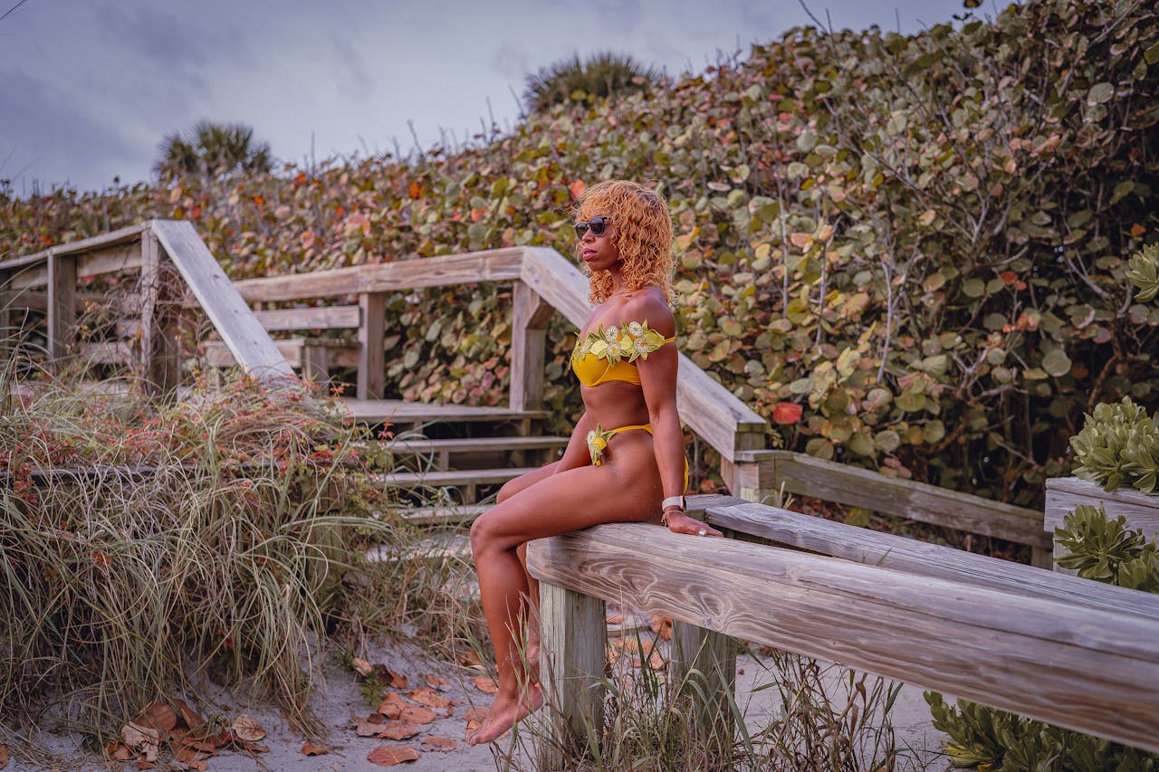 African American woman in yellow bikini sitting on wooden bench outdoors.