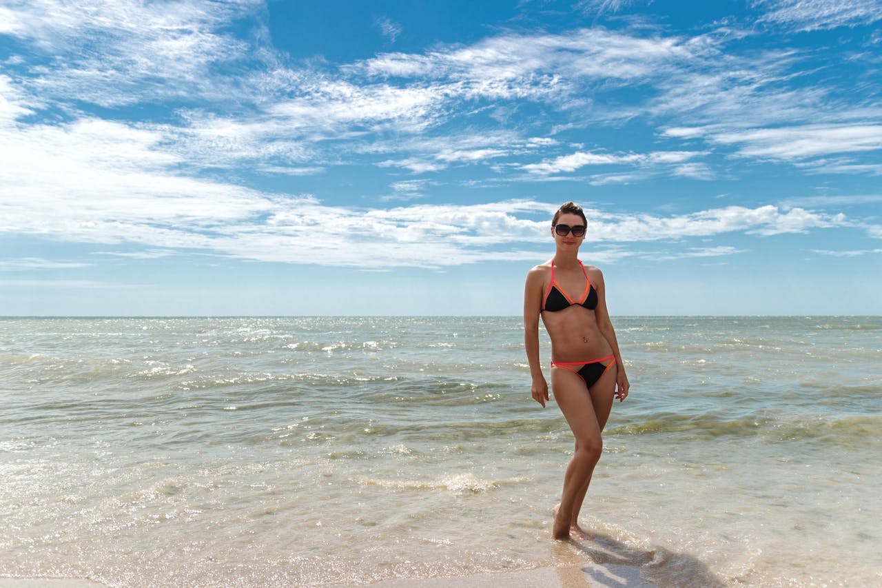 A woman in a bikini stands on the sandy shores of Kyrylivka, Ukraine, under a bright summer sky.