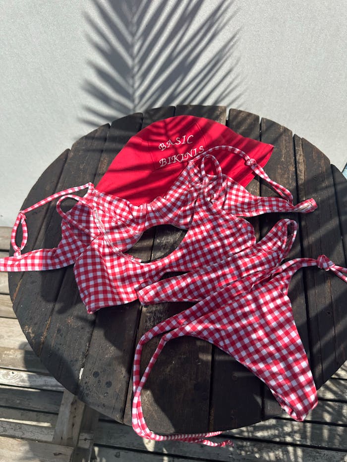 Chic red gingham bikini with cap on wooden outdoor table.
